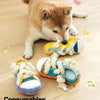 A fluffy dog is lying down next to a pair of squeaky slipper dog chew toys with rope.