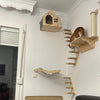 Un árbol de gato de madera de varias capas y poste para rascar montado en una pared blanca con un gato descansando en la estr