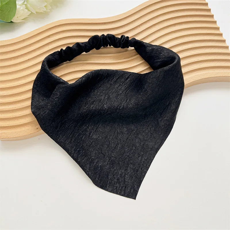 Diadema elástica o pañuelo para el cabello negro sobre una superficie de madera clara.