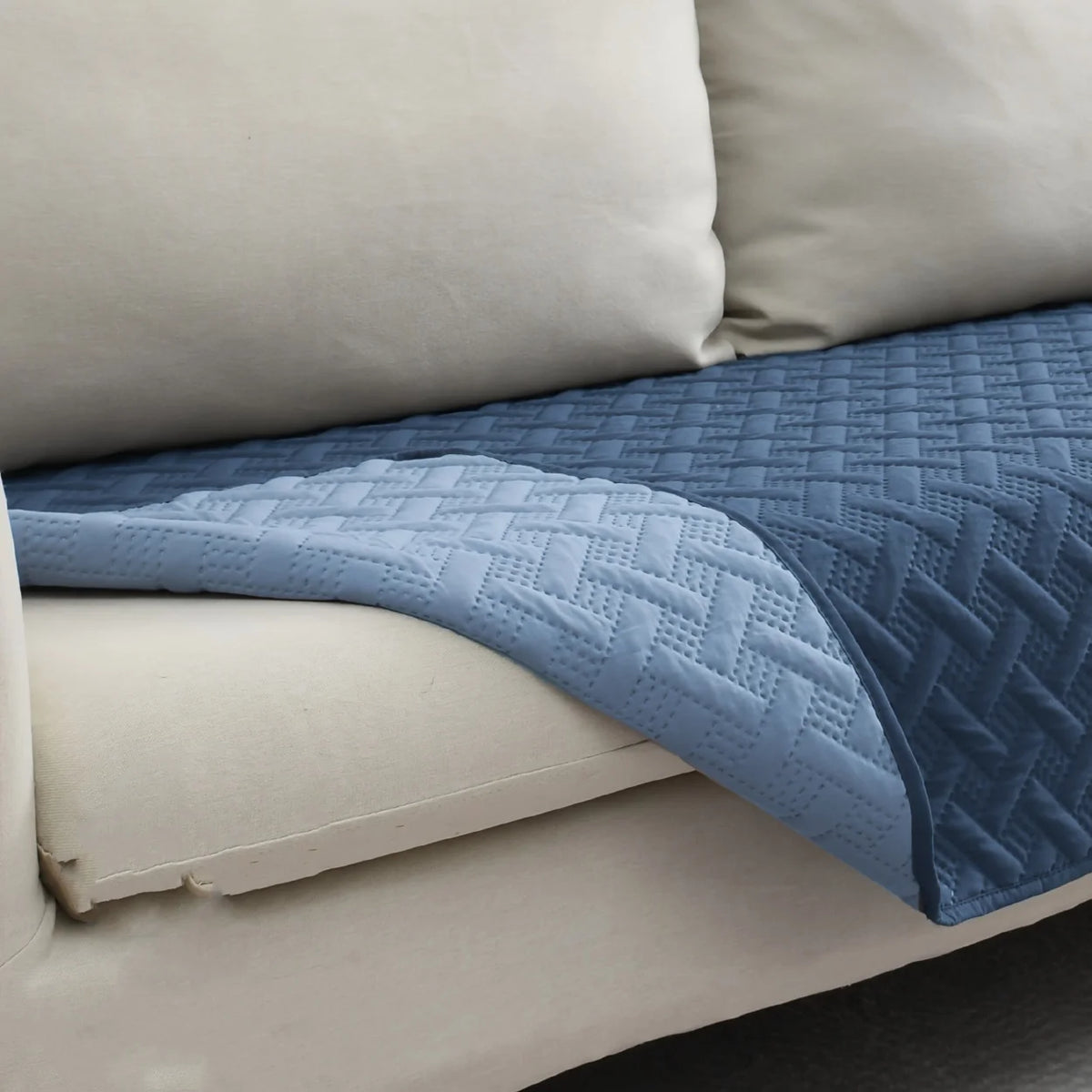 A blue quilted pet mat with a non-slip base is placed on a light-colored sofa cushion.