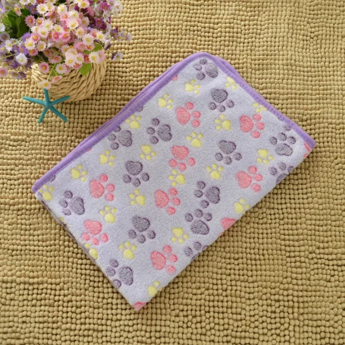 A purple fleece pet bed mat cover with paw prints in pink, yellow, and gray on a beige textured surface.