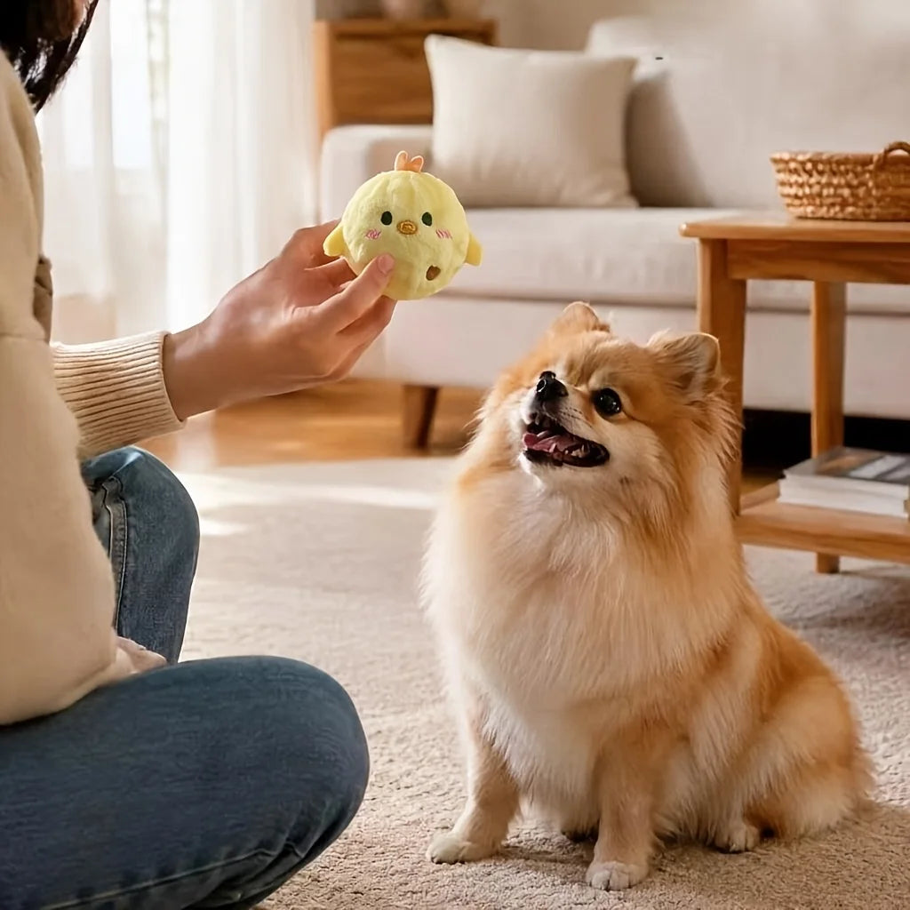 A fluffy apricot-colored squeaky ball shaped like a chick is being held by a person near a golden retriever.