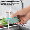 A hand is rinsing a teal cleaning brush under a faucet in a kitchen sink.