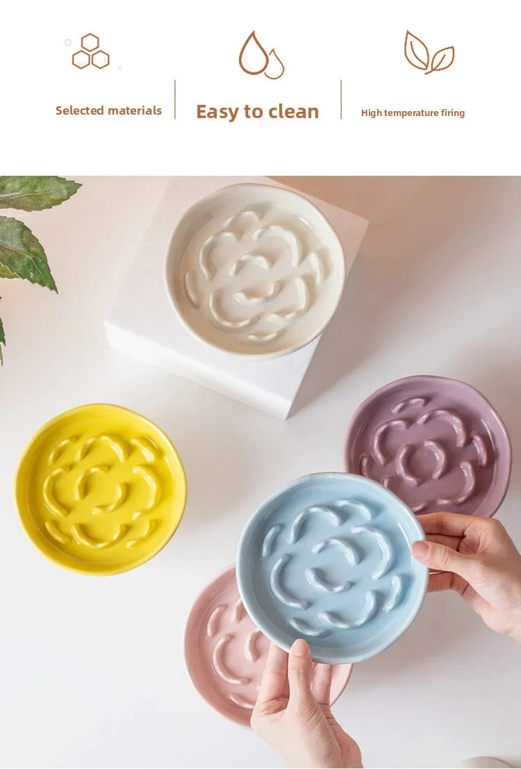 Collection de bols en céramique à nourriture lente pour animaux, dans diverses couleurs pastel, tenus par des mains.