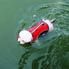 A white dog wearing a red life jacket is swimming in green water.