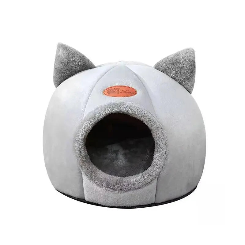 A round gray plush cat cave bed with pointed ears and an oval entrance.