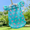 A turquoise pet dress for a small dog featuring a floral print and pearl accents, photographed outdoors.