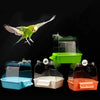 A green parakeet is shown flying near several clear plastic hanging bird baths in various colors.