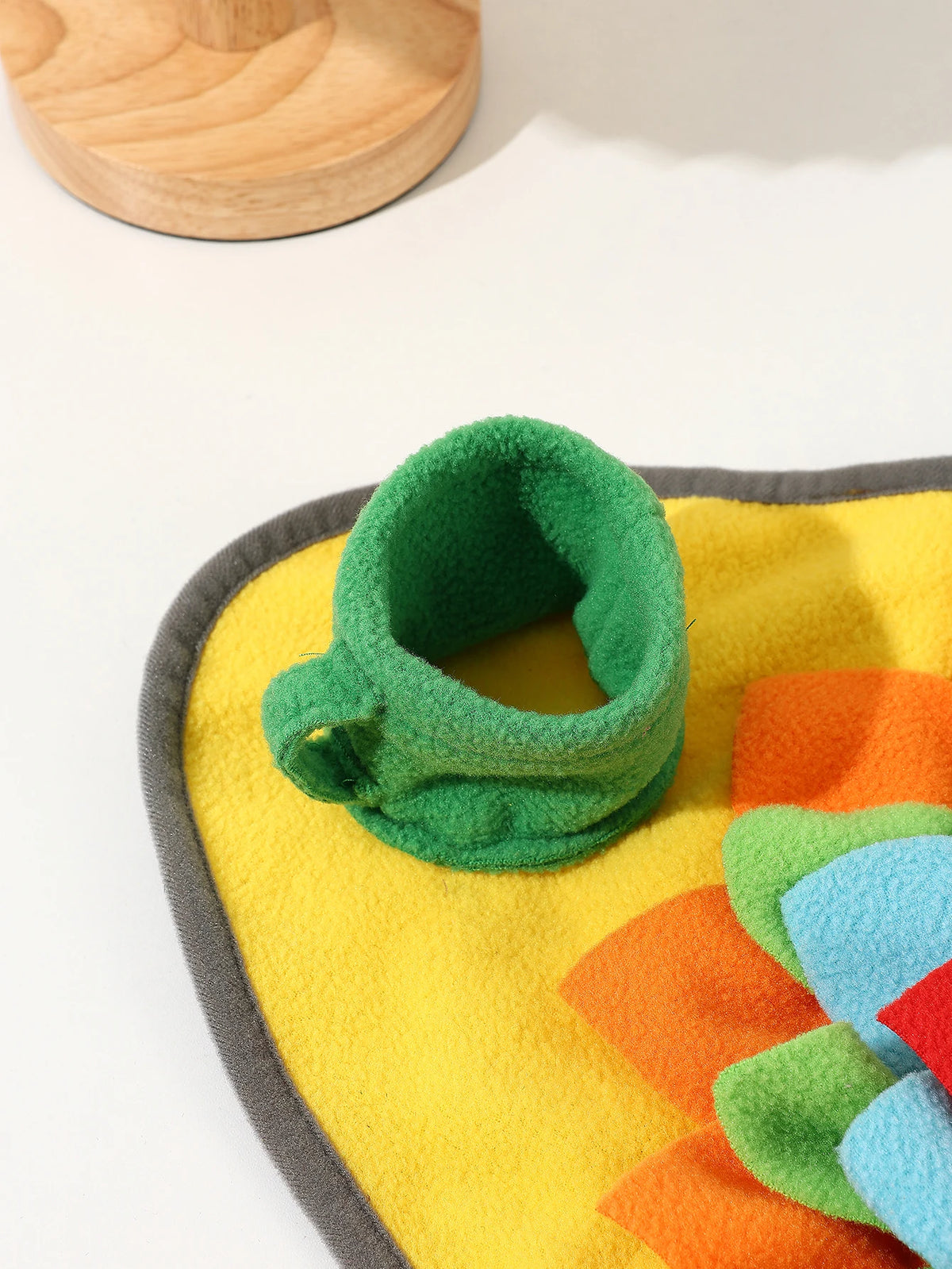 A bright yellow and orange snuffle mat with green fabric pieces for a dog toy.