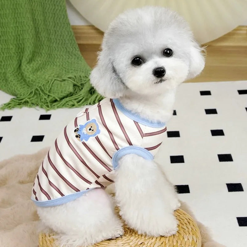 A fluffy white dog wearing a striped cooling vest sits on a light surface.