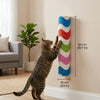 A tabby cat is climbing a vertical, colorful scratching post mounted on a wall.
