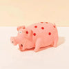 A pink pig squeaky toy with red polka dots lying on a white surface.
