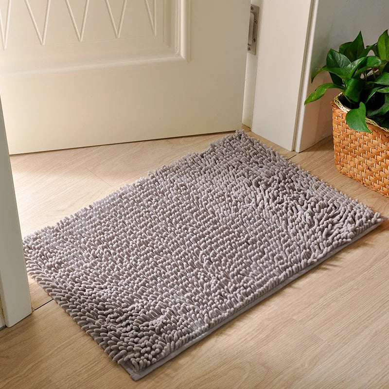 Una alfombra de entrada para mascotas gris y antideslizante colocada sobre un suelo de madera claro junto a un marco de puert