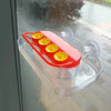 A red and clear suction cup hummingbird feeder with a transparent reservoir filled with yellow nectar flowers.