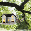 A solar outdoor bird feeder lantern is hanging from a tree branch, illuminating a small wooden house structure.