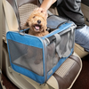 A person is placing a small, light brown dog into a blue and gray breathable mesh pet carrier bag inside a car.