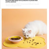 A white cat is eating dry pet food scattered on a yellow silicone feeding mat.