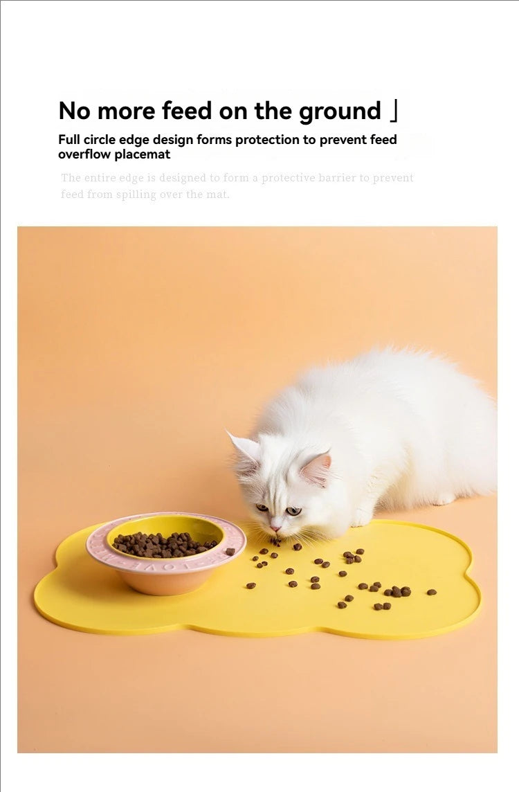 A white cat is eating dry pet food scattered on a yellow silicone feeding mat.