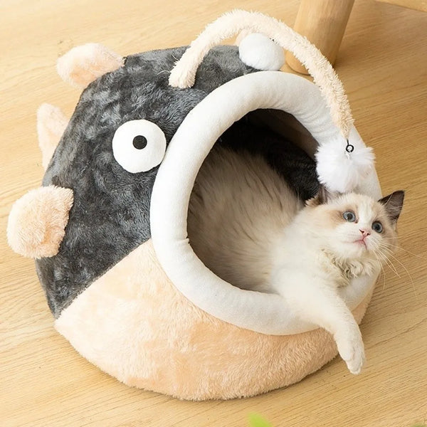 A plush cartoon lantern fish cat bed shaped like a fish with an arched opening, featuring a white kitten inside.