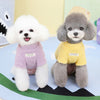 Dos perros de peluche vistiendo suéteres amarillos y morados, sentados sobre un fondo de paisaje verde