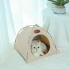 A beige foldable pet tent for cats is shown with an entrance, resting on a white fluffy surface.