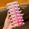 Eine Hand hält eine Packung bunter rosa und korallfarbener Stoff-Haarspangen zum Basteln.