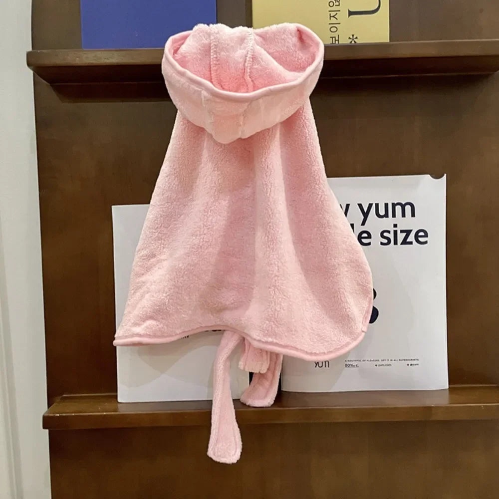 A pink, fluffy multi-purpose pet bath robe for dogs is displayed on a wooden shelf.