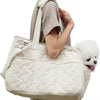 A person is holding a beige quilted portable pet carrier bag with a white fluffy dog.