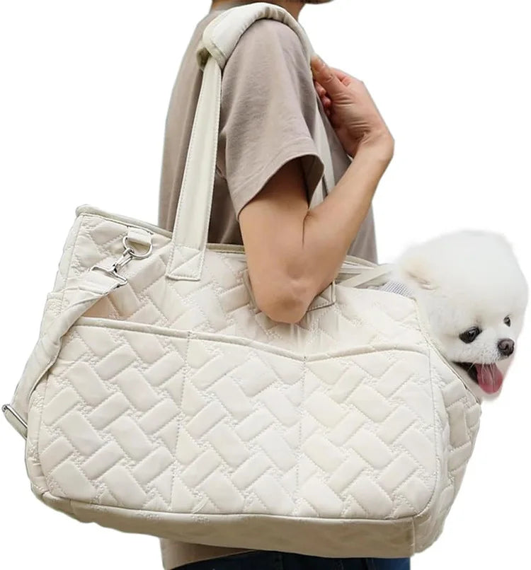 A person is holding a beige quilted portable pet carrier bag with a white fluffy dog.