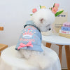 A fluffy white dog wearing a pink princess style denim jacket with a crown and bow.