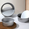 A set of round aluminum cake pans and a circular pan resting on a wooden board against a textured background.