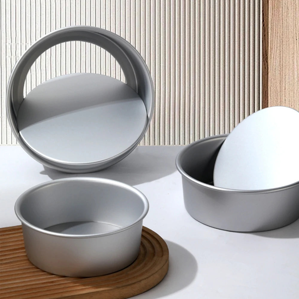 A set of round aluminum cake pans and a circular pan resting on a wooden board against a textured background.