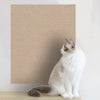 A white and gray cat is sitting on a beige self-adhesive scratching mat designed for furniture protection.