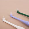 Three soft bristle pet toothbrushes in white, purple, and green displayed on a beige background.