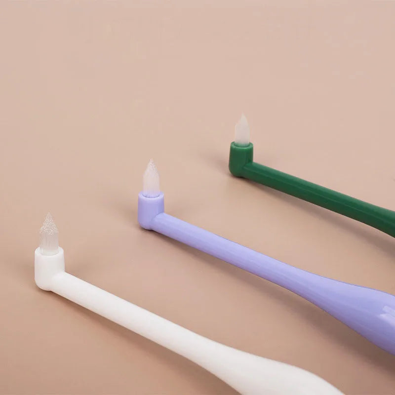 Three soft bristle pet toothbrushes in white, purple, and green displayed on a beige background.