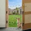 A vertical black metal pet safety gate is installed in a wooden door frame, separating an indoor area from a grassy outdoor y