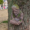 A resin sculpture of a monkey hugging its hands carved into the bark of a tree.
