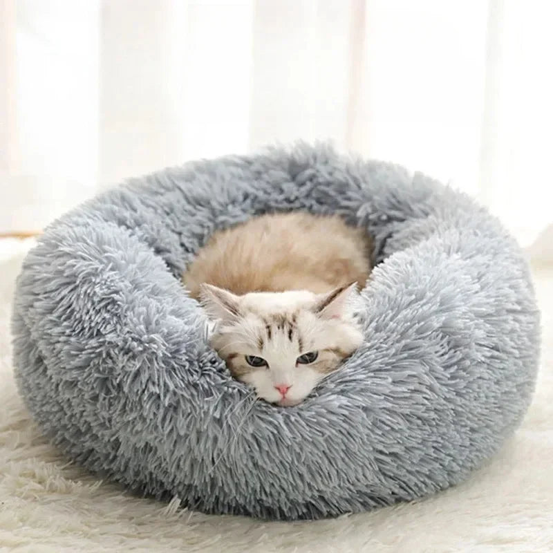 A fluffy gray faux fur round bed with a cat nestled inside.