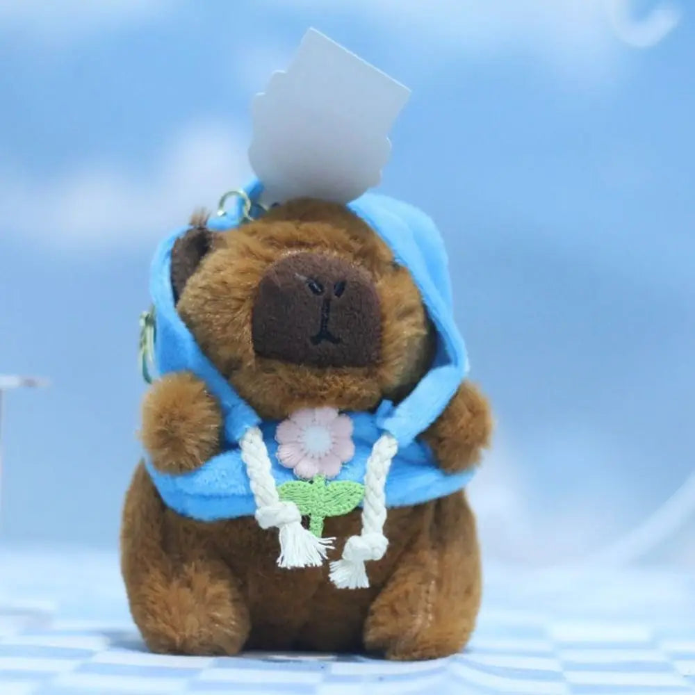 A brown capybara plush doll wearing a blue hoodie with white wings.
