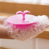 A hand holds a pink silicone hair and scalp massage brush with a silicone dome on a white mesh surface.