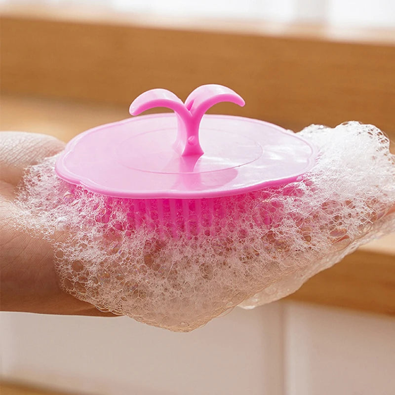 A hand holds a pink silicone hair and scalp massage brush with a silicone dome on a white mesh surface.
