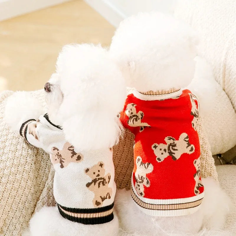 Un suéter rojo para perro con estampado de oso junto a un juguete de perro blanco y esponjoso.