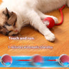 A white and tabby cat is lying on a wooden floor next to an interactive cat toy ball with a motion sensor.