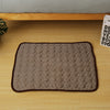 A rectangular gray quilted cooling mat with brown trim resting on a wooden surface.