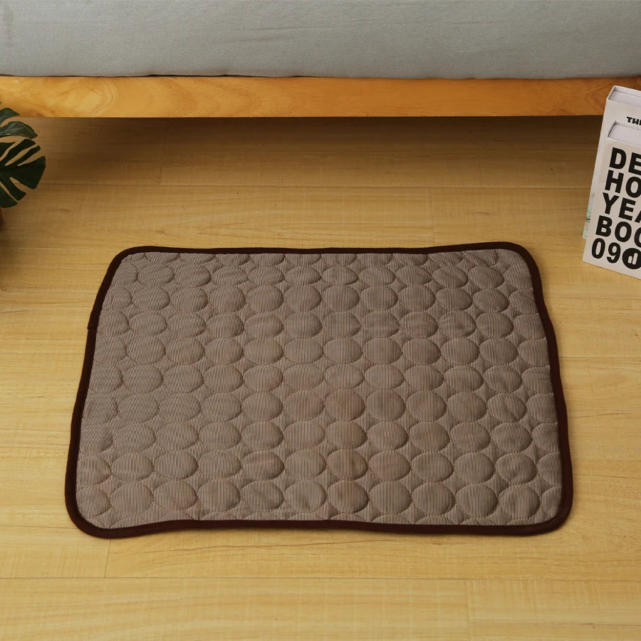A rectangular gray quilted cooling mat with brown trim resting on a wooden surface.
