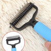 A black pet detangling comb with a blue handle is shown resting on a white, fluffy surface.