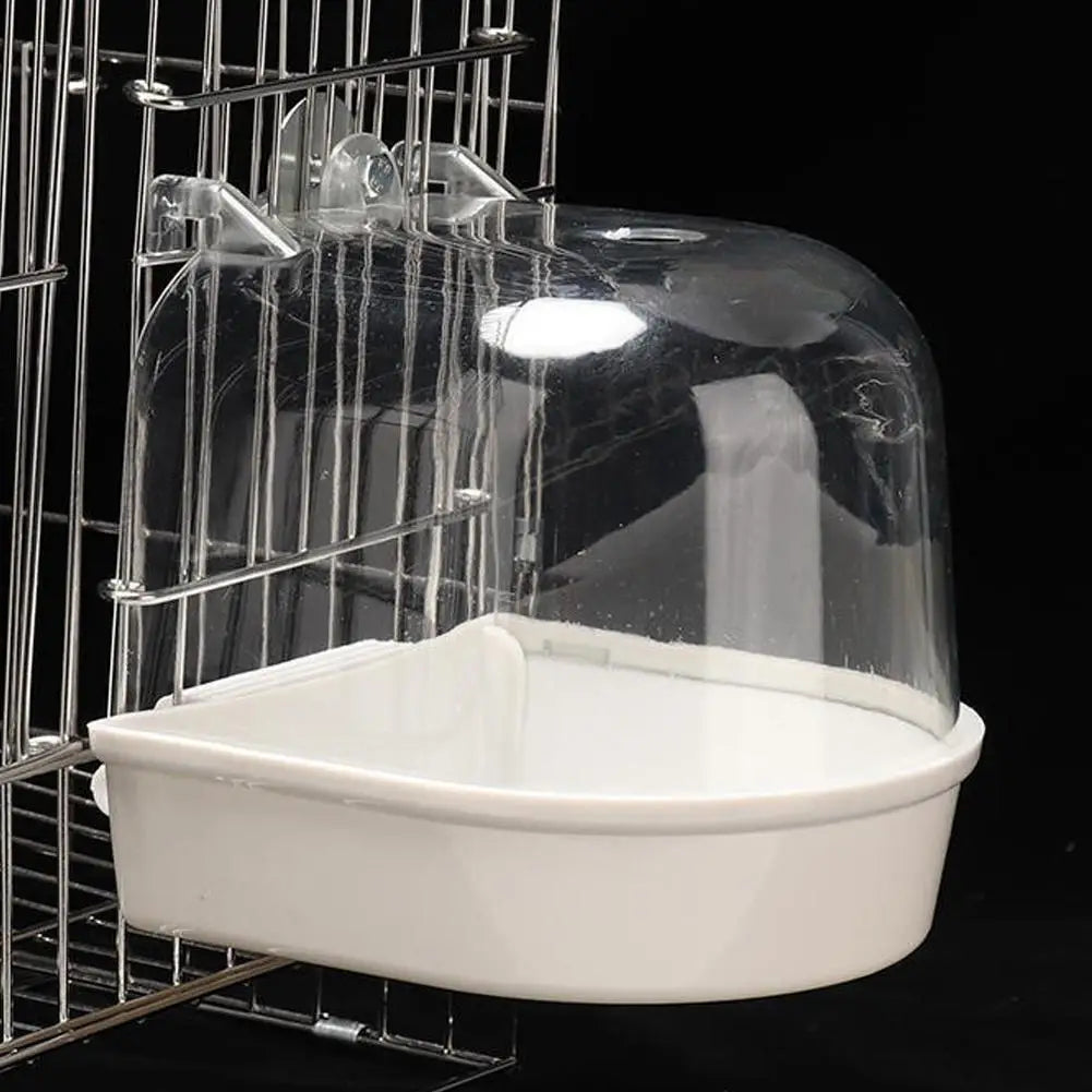 A clear plastic hanging bird bath for parakeets is shown inside a wire cage.
