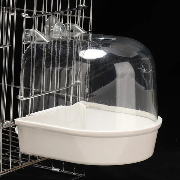 A clear plastic hanging bird bath for parakeets is shown inside a wire cage.
