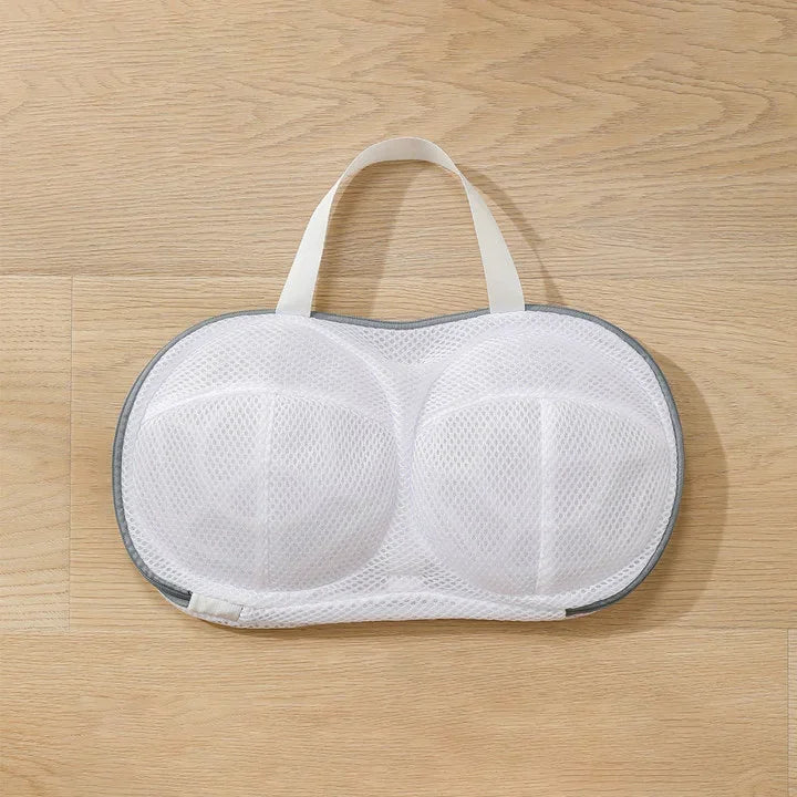 Bolsa de lavado de malla blanca reutilizable con asa, sobre una superficie de madera clara.