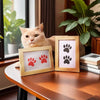 A ginger cat sits next to wooden frames displaying paw print designs for a pet keepsake kit.